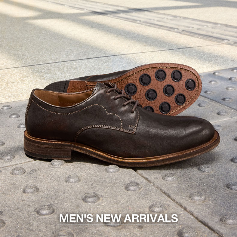 Pair of dark brown leather men's dress shoes displayed on a city sidewalk, with one shoe showing the textured rubber outsole. Text reads &ldquo;Men's New Arrivals.&rdquo;